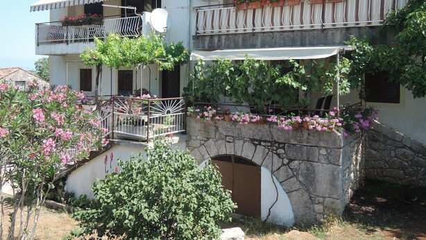 A two-story building with a stone archway, balconies with flower boxes, and a small garden area. - Apartment Sabina & Grapes (Malinska-Dubasnica)