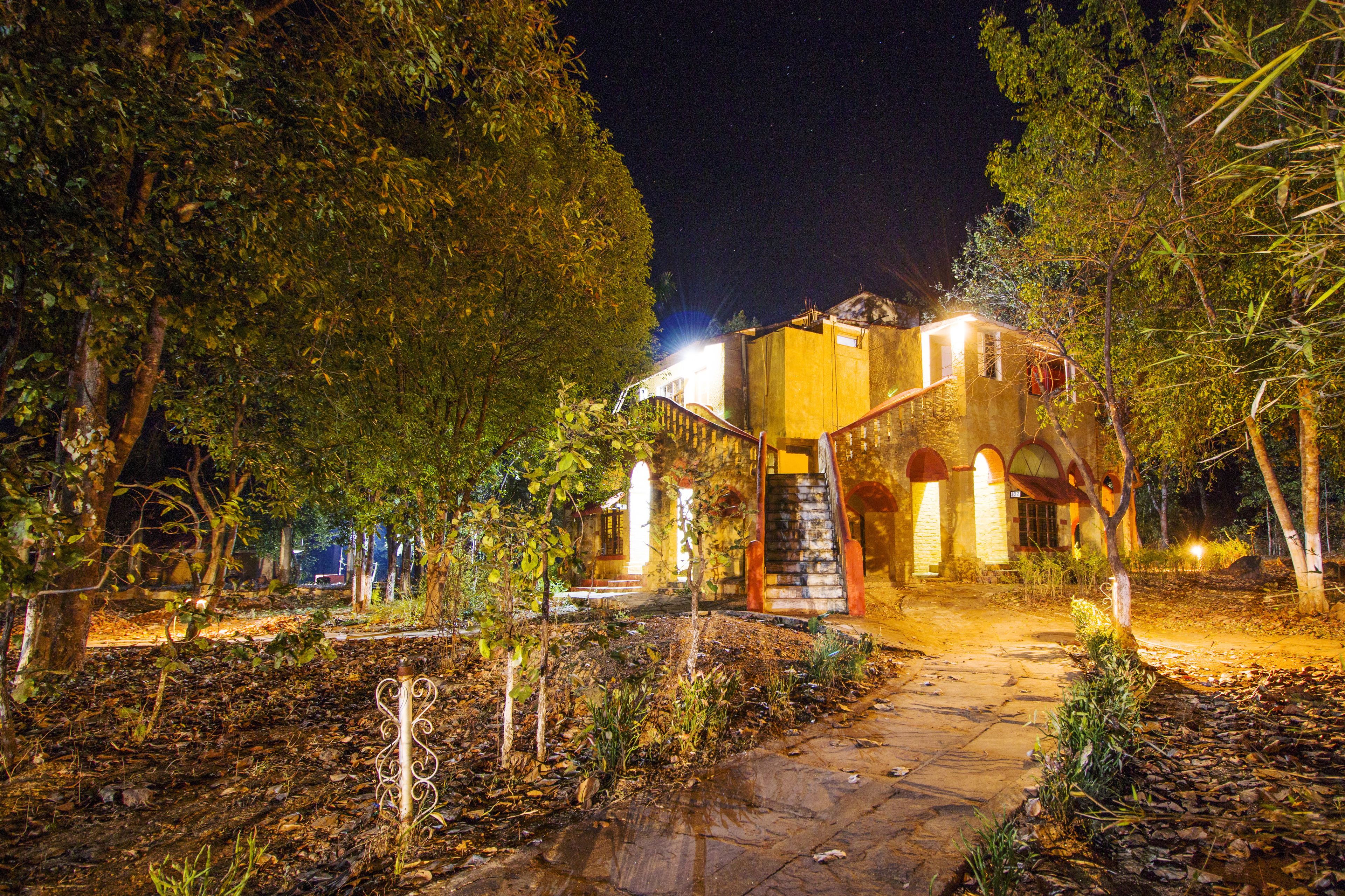Um edifício com uma escadaria de pedra que leva a uma porta, cercado por árvores e um caminho de pedra.