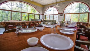 Un comedor con mesas dispuestas para el servicio, amplias ventanas en arco y una pared de ladrillo.