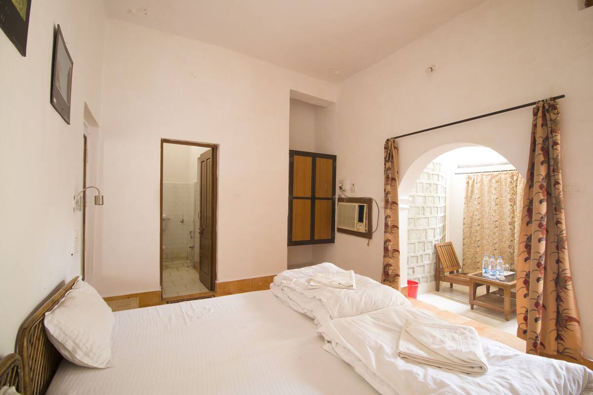A hotel room with a bed, a chair, a table with water bottles, and a shower area.