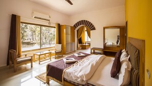 Habitación de hotel con cama, escritorio, silla, ventana con cortinas, ventilador de techo y espejo.