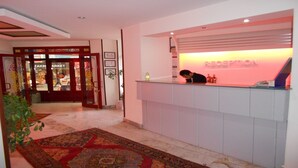 A reception area with a red-lit desk, a patterned carpet, and a store entrance with glass doors. - Nas Hotel (Karaman)
