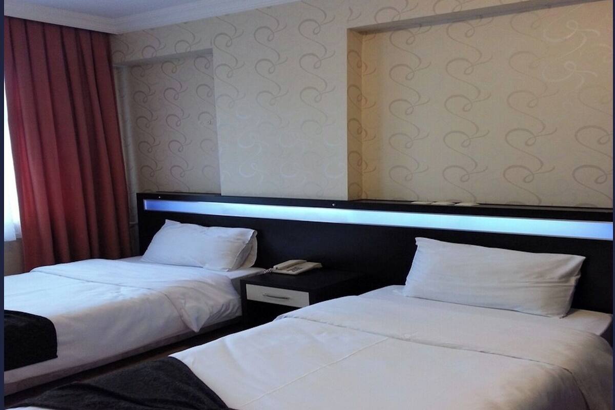 A hotel room with two beds, a nightstand with a phone, and a window with curtains.