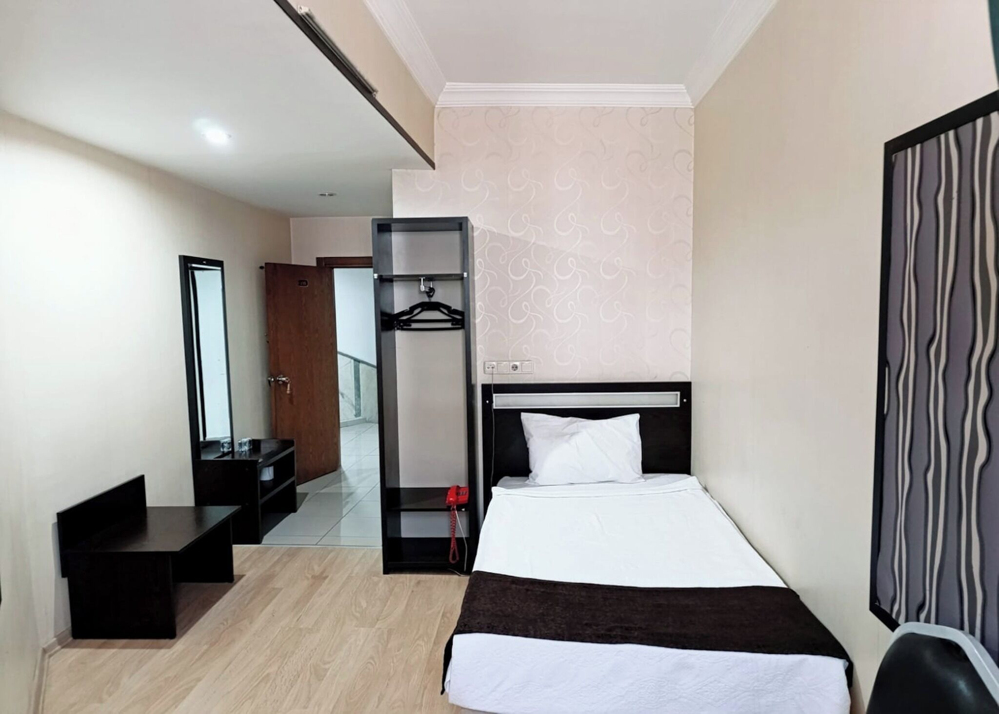 Habitación de hotel con cama, armario, espejo, escritorio y perchero.