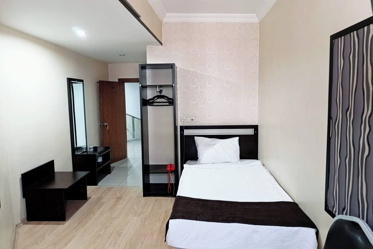 A hotel room with a bed, a wardrobe, a mirror, a desk, and a hanging coat rack.