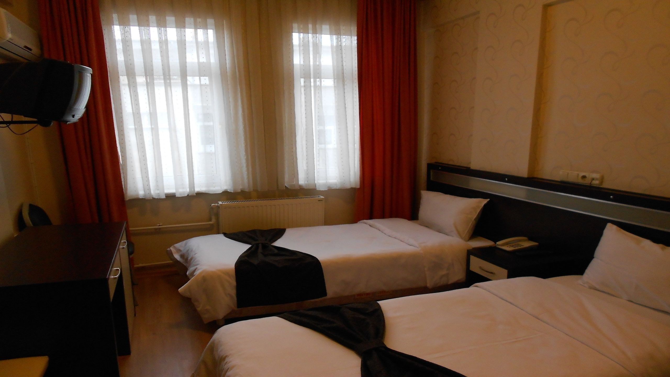 A hotel room with two beds, a desk, a telephone, and a radiator.
