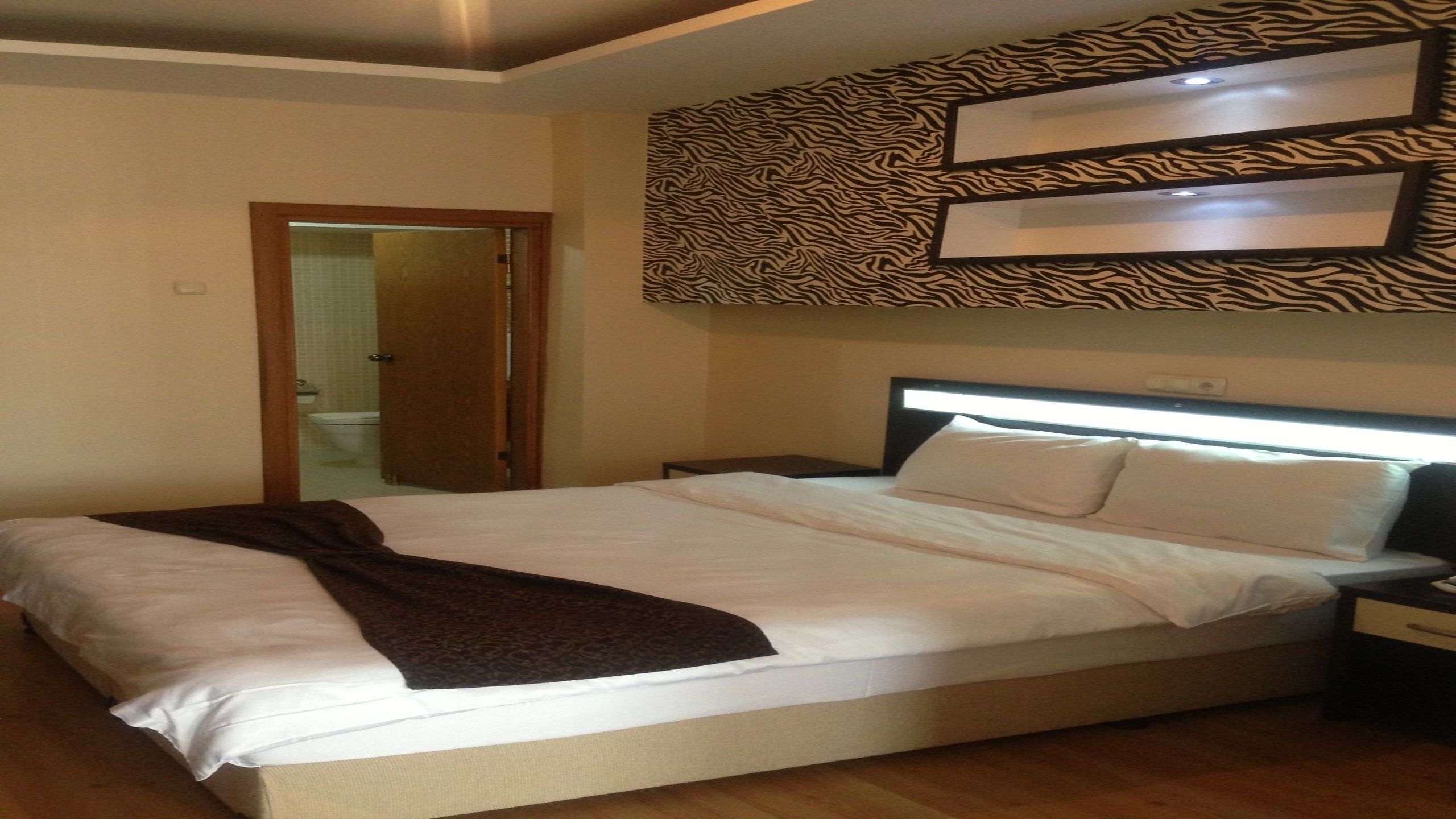 Una habitación de hotel con cama, mesita de noche, pared con estampado de cebra y puerta que da a un baño.