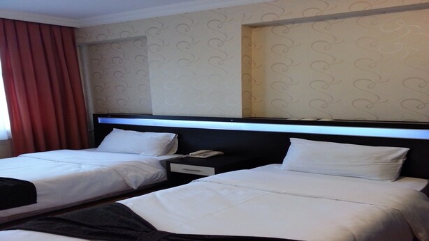 A hotel room with two beds, a nightstand, and a telephone. - Nas Hotel (Karaman)