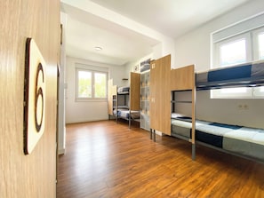 A room with bunk beds, a wooden floor, a window, and a door with a number sign. -  North Surf House (Gijon)