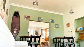A dining area with wooden tables and chairs, a surfboard decoration, and framed artwork on the walls. -  North Surf House (Gijon)
