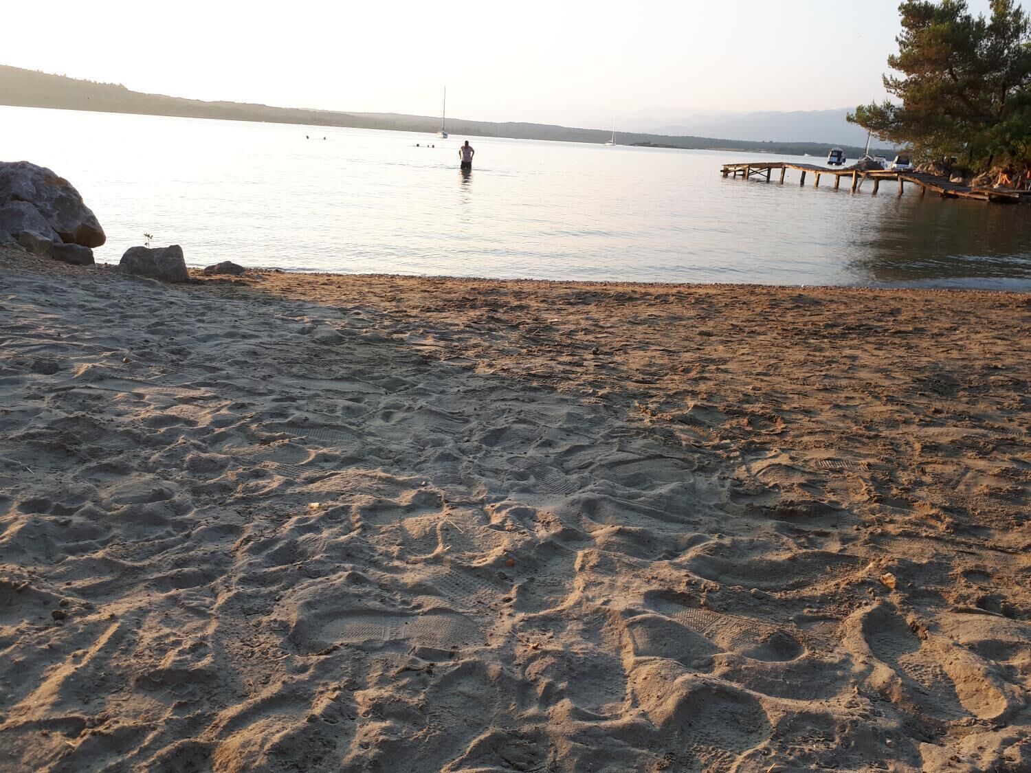 A sandy beach with footprints leading to a wooden dock.