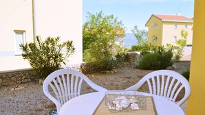 An outdoor seating area with two white plastic chairs and a table, set against a backdrop of a yellow building and greenery. - Apartment Sunshine (Dobrinj)