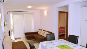 A compact living space with a sofa, a dining table, and a bed. - Apartment Sunshine (Dobrinj)