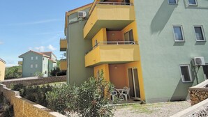 A multi-story residential building with balconies, air conditioning units, and a small outdoor seating area. - Apartment Sunshine (Dobrinj)