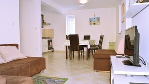 A living room with a sofa, a TV, and a dining area with chairs and a table. - Apartment Sunshine (Dobrinj)