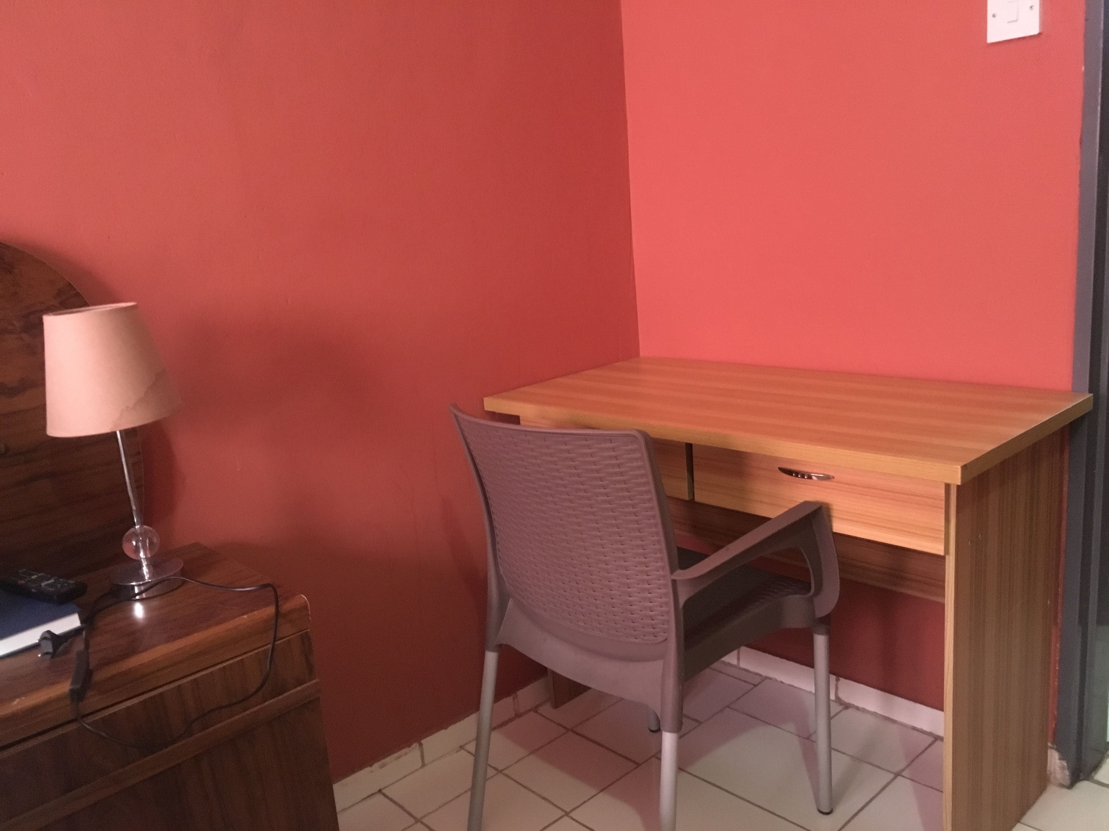 A room with a wooden desk, a chair, a lamp, and a dresser.