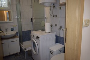Une petite salle de bain équipée d’un lave-linge, d’un évier et de toilettes.