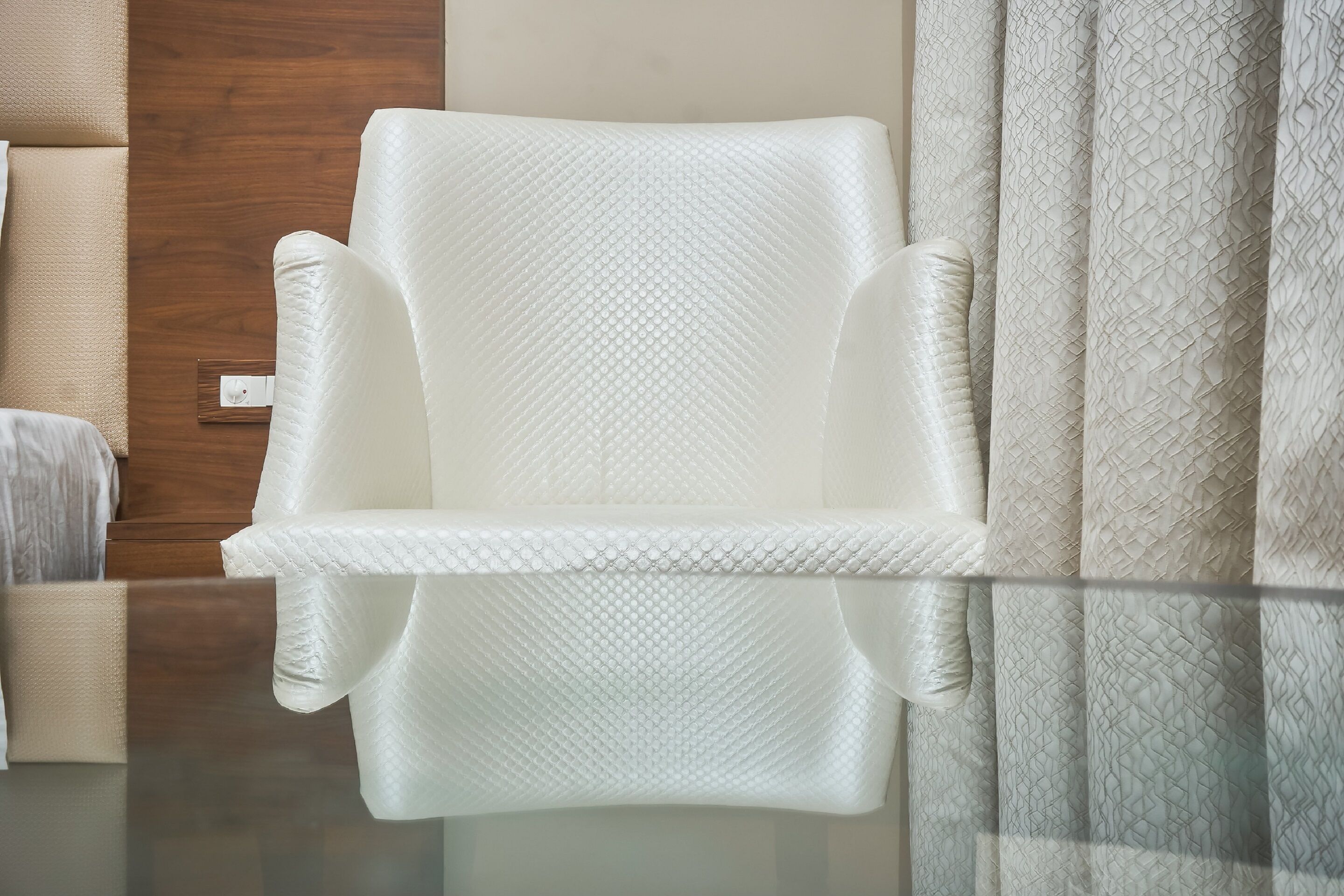 A white armchair with a textured fabric, positioned next to a wooden door and a patterned curtain.