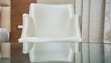 A white armchair with a textured fabric, positioned next to a wooden door and a patterned curtain.