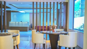 A modern hotel lobby with a reception desk, a seating area with a sofa and chairs, and a dining area with a round table and chairs. - Ganpati Hotel (Reasi)