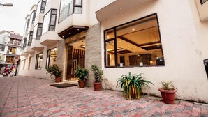 A hotel entrance with a modern design, featuring a large glass window and potted plants. - Ganpati Hotel (Reasi)