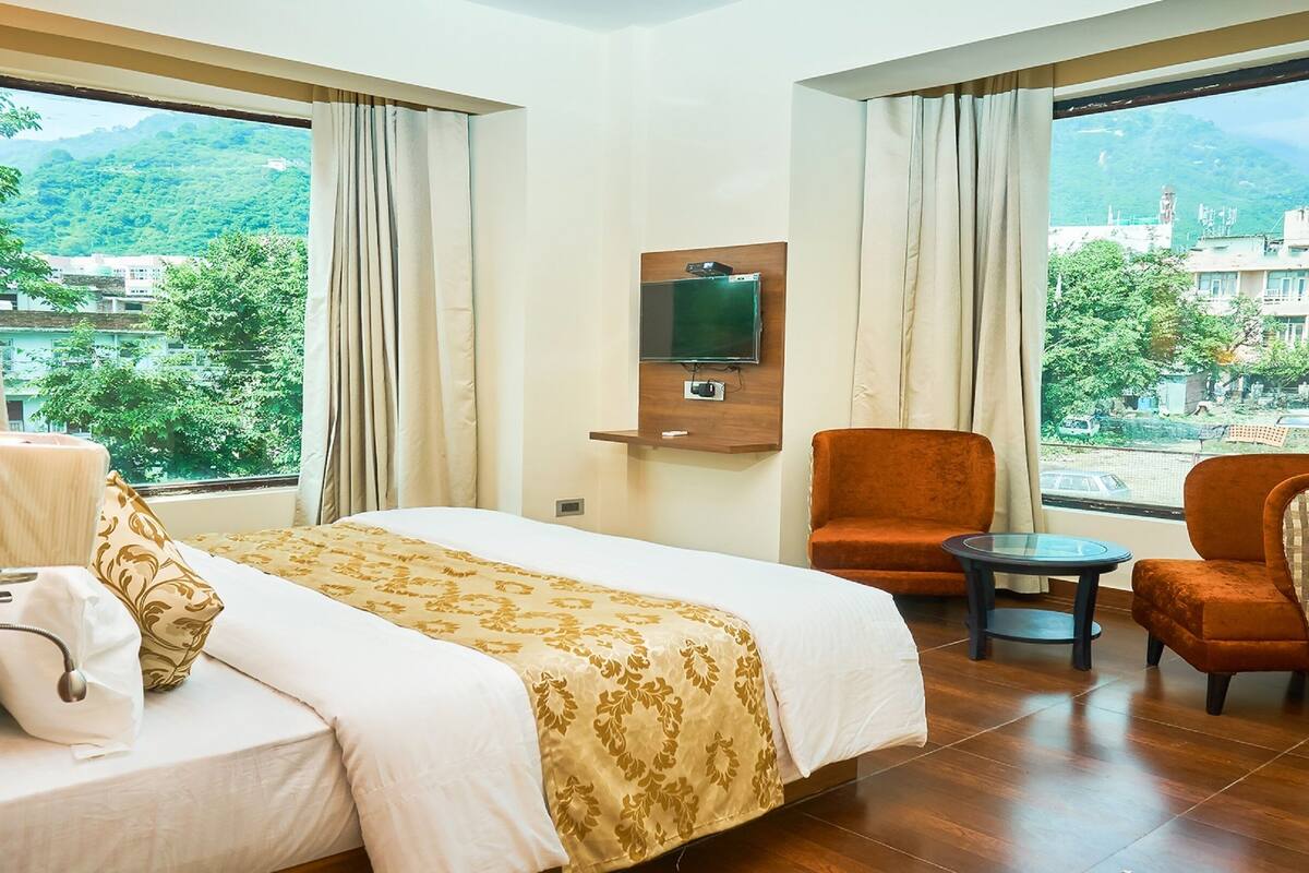 Habitación de hotel con cama, televisión montada en la pared, una silla y una mesita.