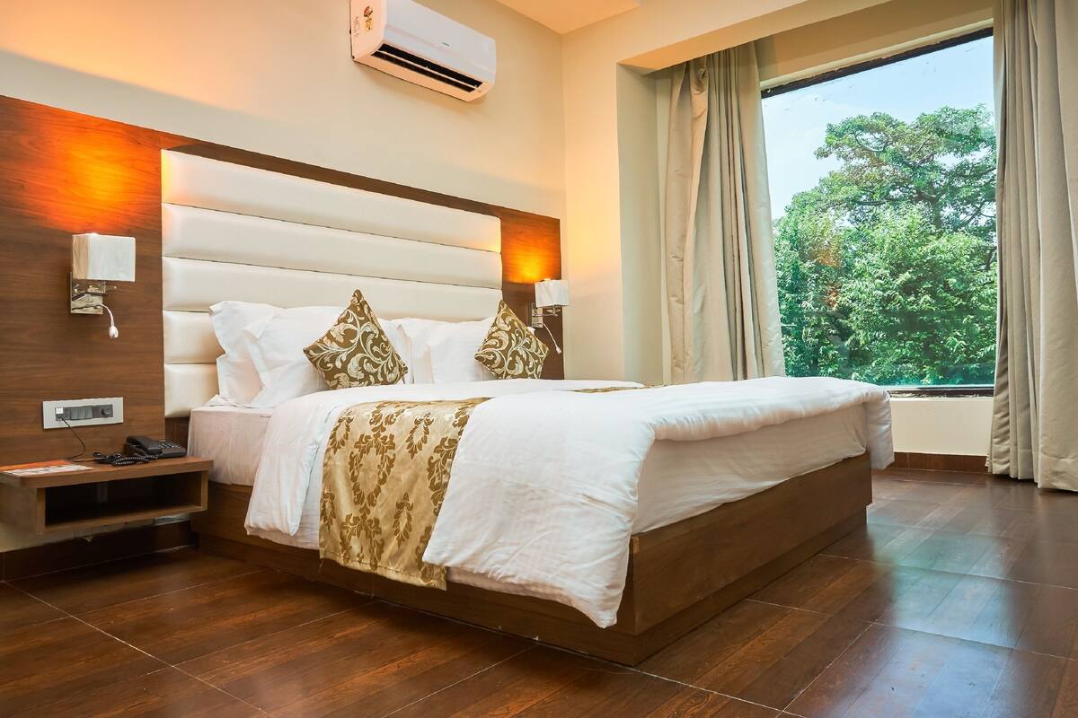 Una habitación de hotel moderna con una cama grande, cabecera de madera, lámparas de noche, mesita de noche y una ventana con cortinas.