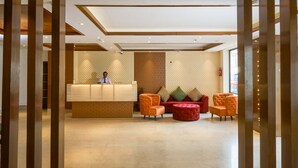 A reception area with a reception desk, cushioned seating, and a patterned wall. - Ganpati Hotel (Reasi)
