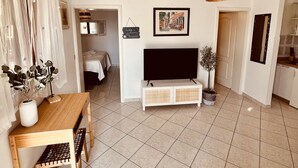 Een woonkamer met een televisie, een eettafel en een bank. Er staat een plant en er hangt een lamp.