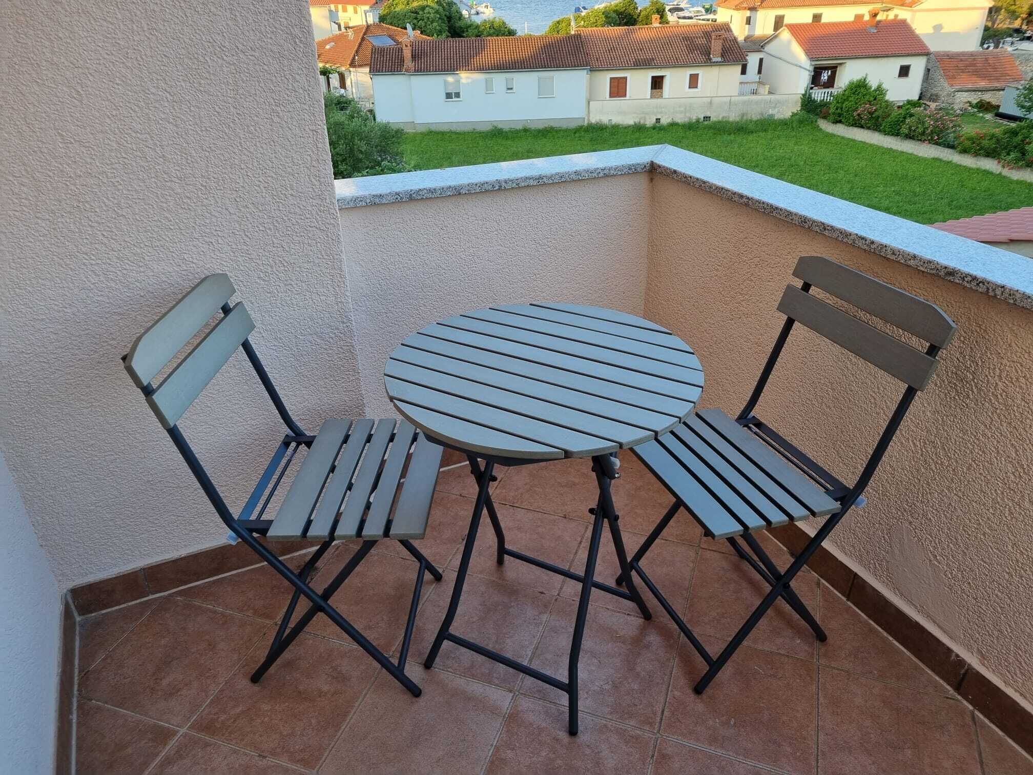 Un pequeño balcón exterior con una mesa redonda y dos sillas.