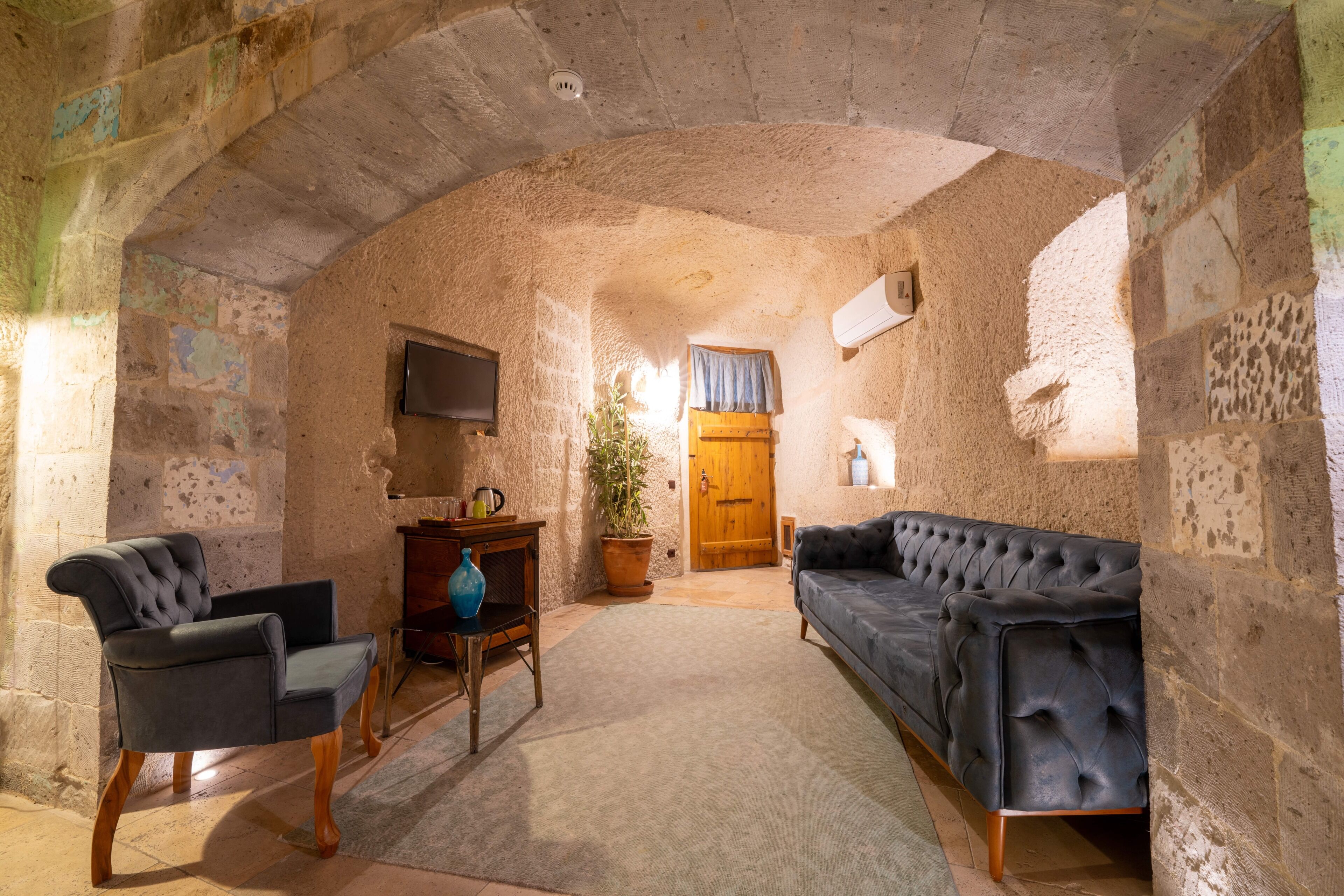 A stone-walled room with a sofa, armchair, and a television on the wall.