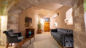 A stone-walled room with a sofa, armchair, and a television on the wall.