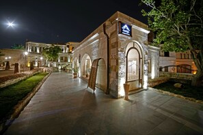 A historic building with a sign reading "aceign espaaCola" at night, featuring arched walkways and a paved courtyard. - Design Cave Hotel (Nevsehir)
