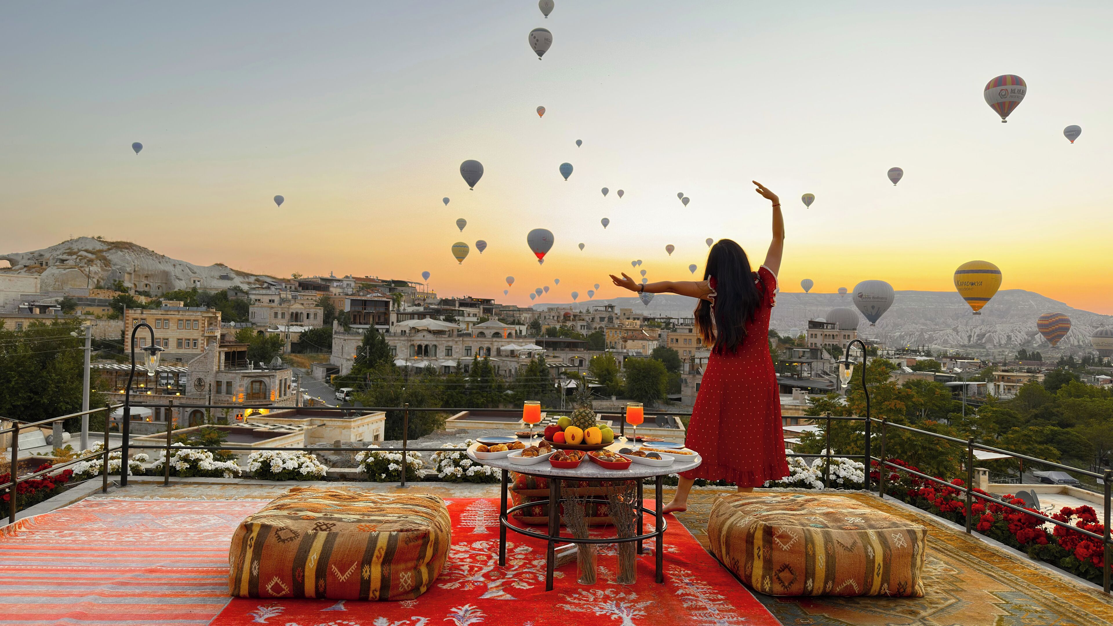 Eine Frau auf einer Dachterrrasse mit Blick auf eine Stadtlandschaft, am Himmel schwebende Heißluftballons.