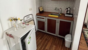 A compact kitchen with wooden cabinets, a small refrigerator, and a tiled backsplash. - Siren Pansiyon (Foça)