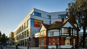 A modern building with a sign that reads "INSPIRING AND BEING INSPIRING" and a traditional building with a red brick facade. - B6 Medium Studio (London)