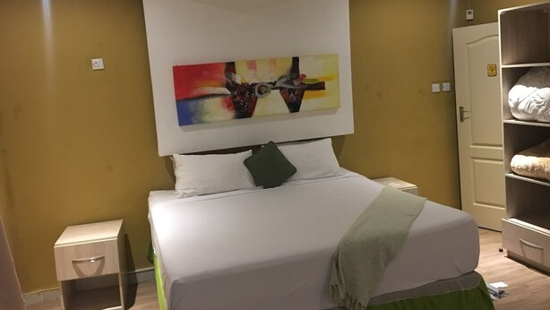 Un dormitorio ordenado con cama, mesita de noche, armario y un cuadro abstracto colorido en la pared.