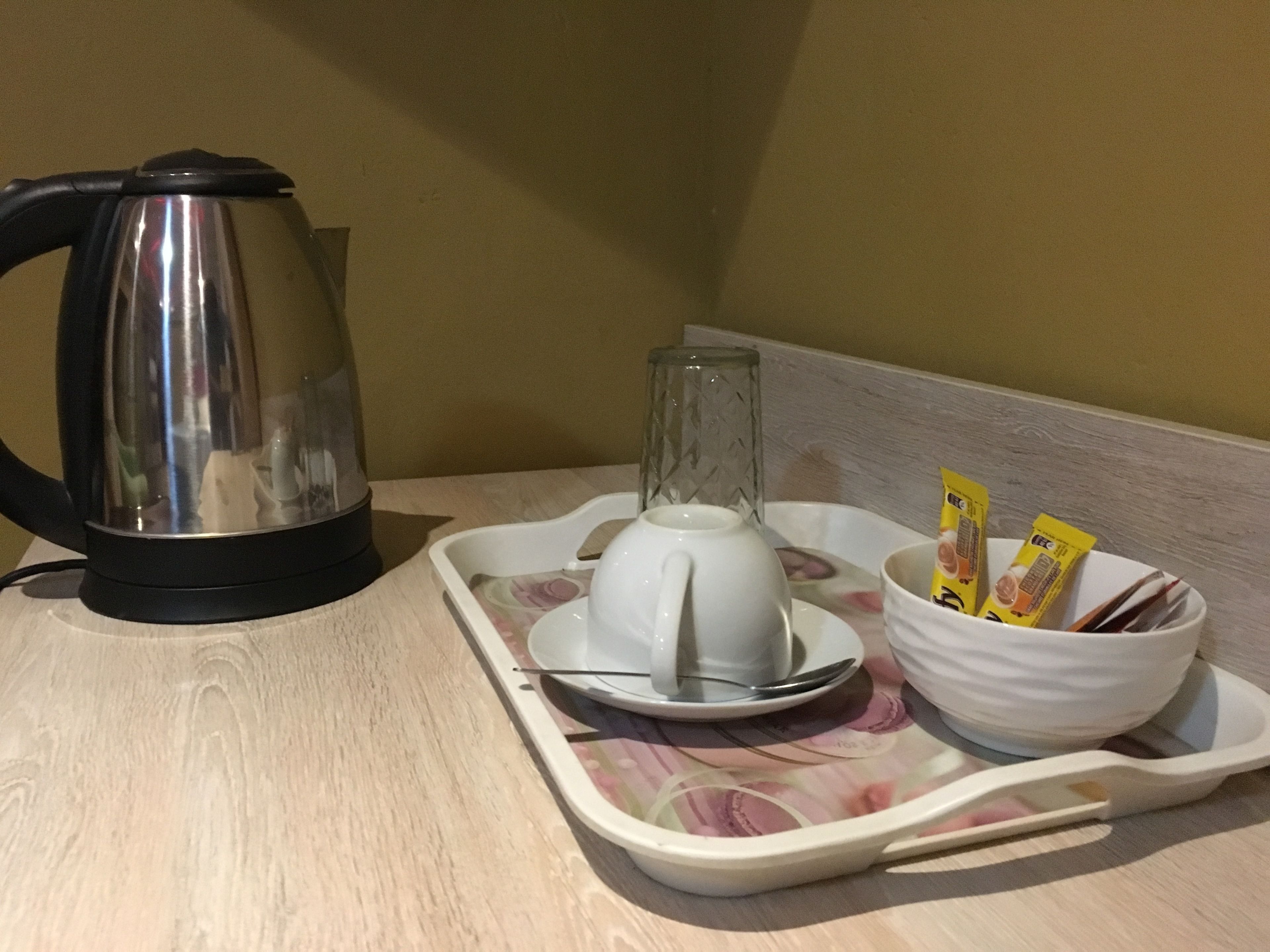 Uma bandeja com um bule, um jarro de vidro, uma xícara, uma colher e pacotes de lanches.