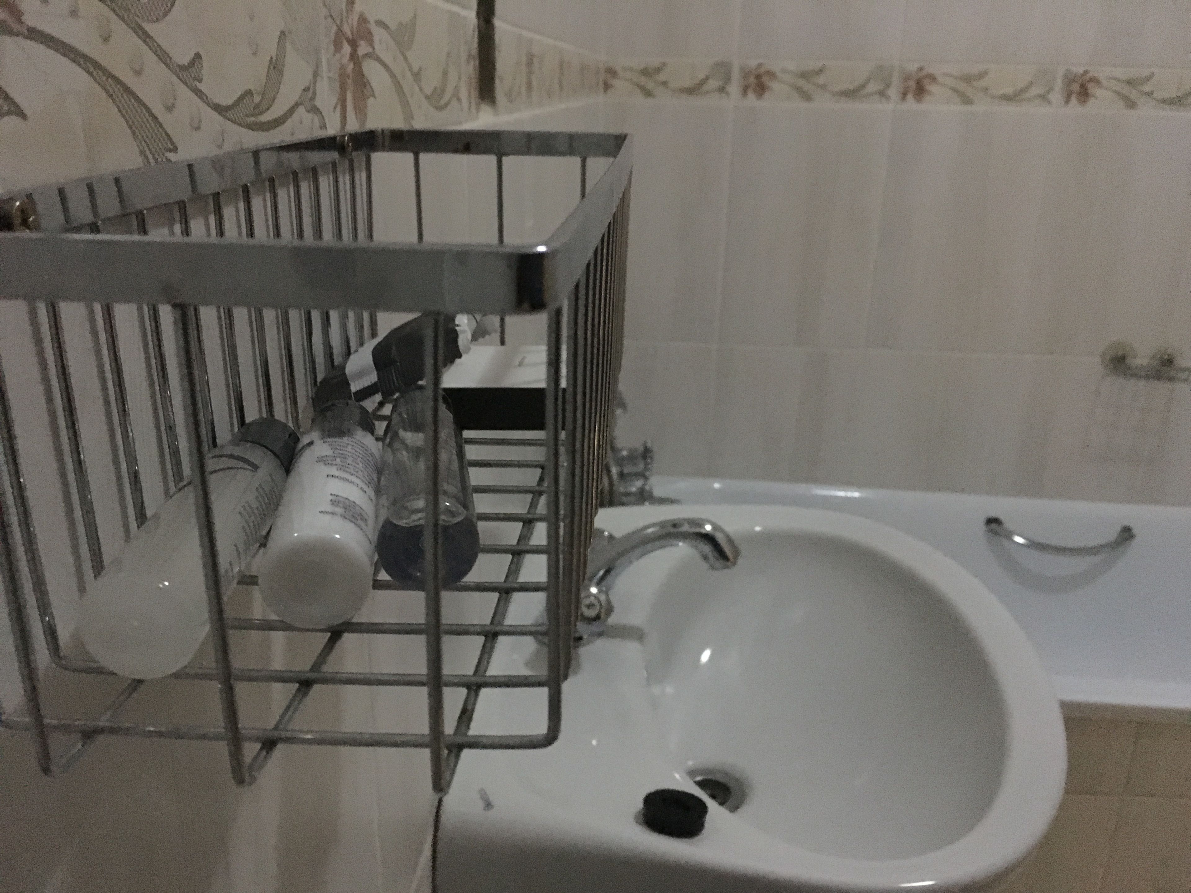 Un baño con un lavamanos blanco, un estante metálico con artículos de tocador y una bañera.