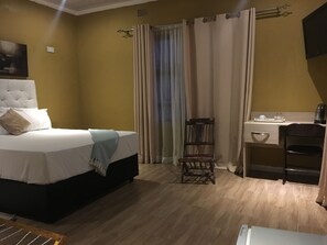 A hotel room with a bed, a desk, a chair, and a window with curtains.