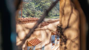 A view through a window with a decorative frame, revealing a building with terracotta roof tiles and a hillside in the background.