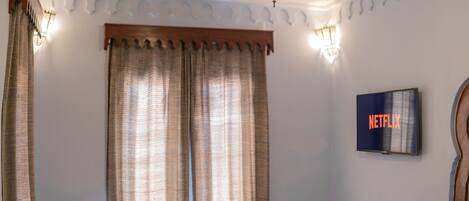 A bedroom with a bed, curtains, a wall-mounted TV, and a decorative ceiling light.