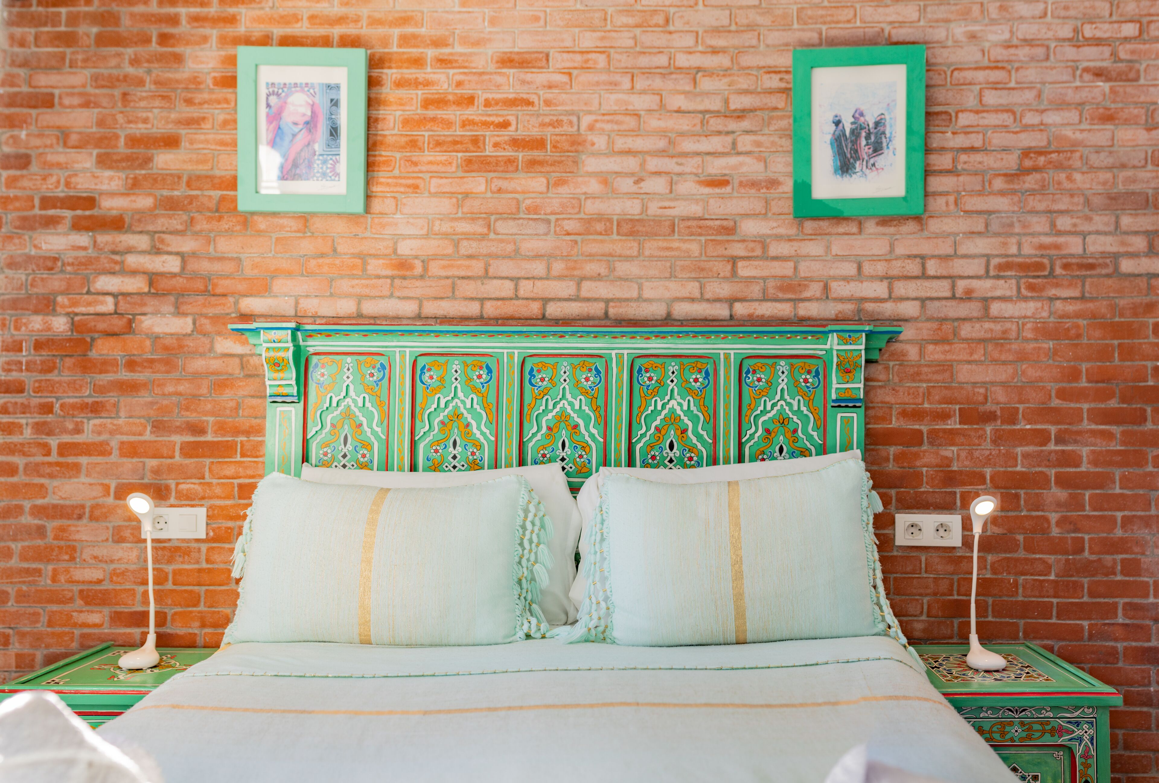 A bed with a green headboard, two pillows, and two bedside tables with lamps.