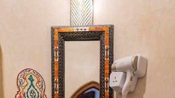 A bathroom with a decorative mirror, a hairdryer, a sink with a blue basin, and a soap dispenser.