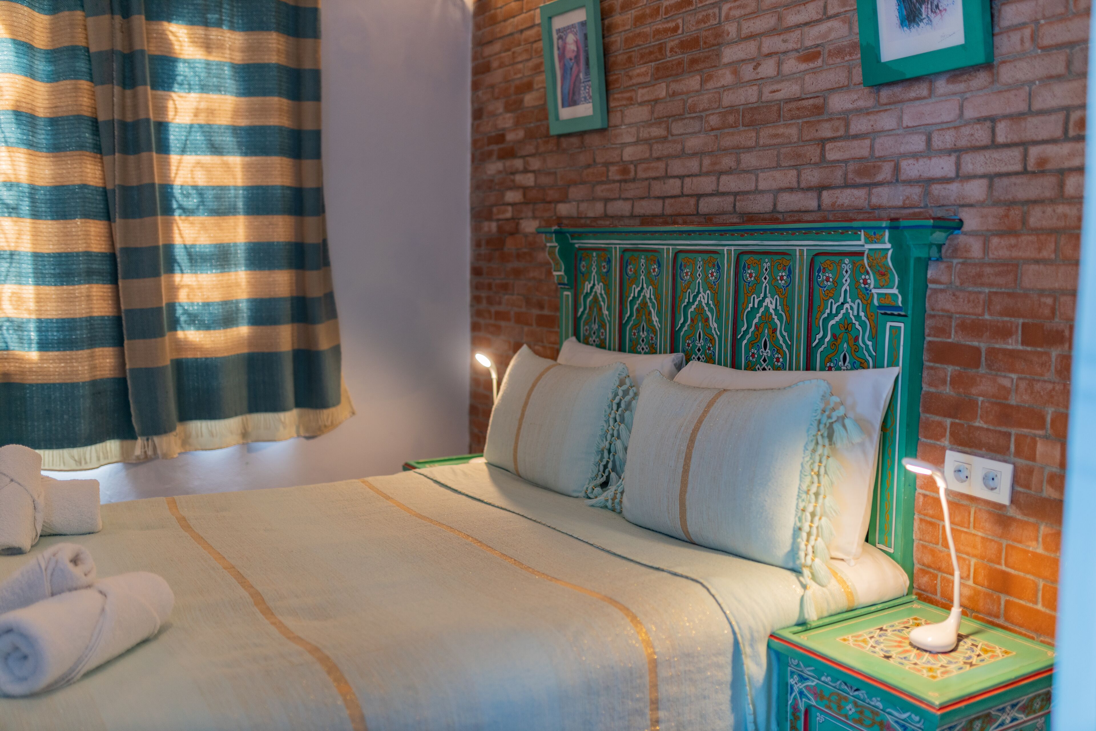 A neatly made bed with a striped curtain, a green headboard, and a bedside table with a lamp.
