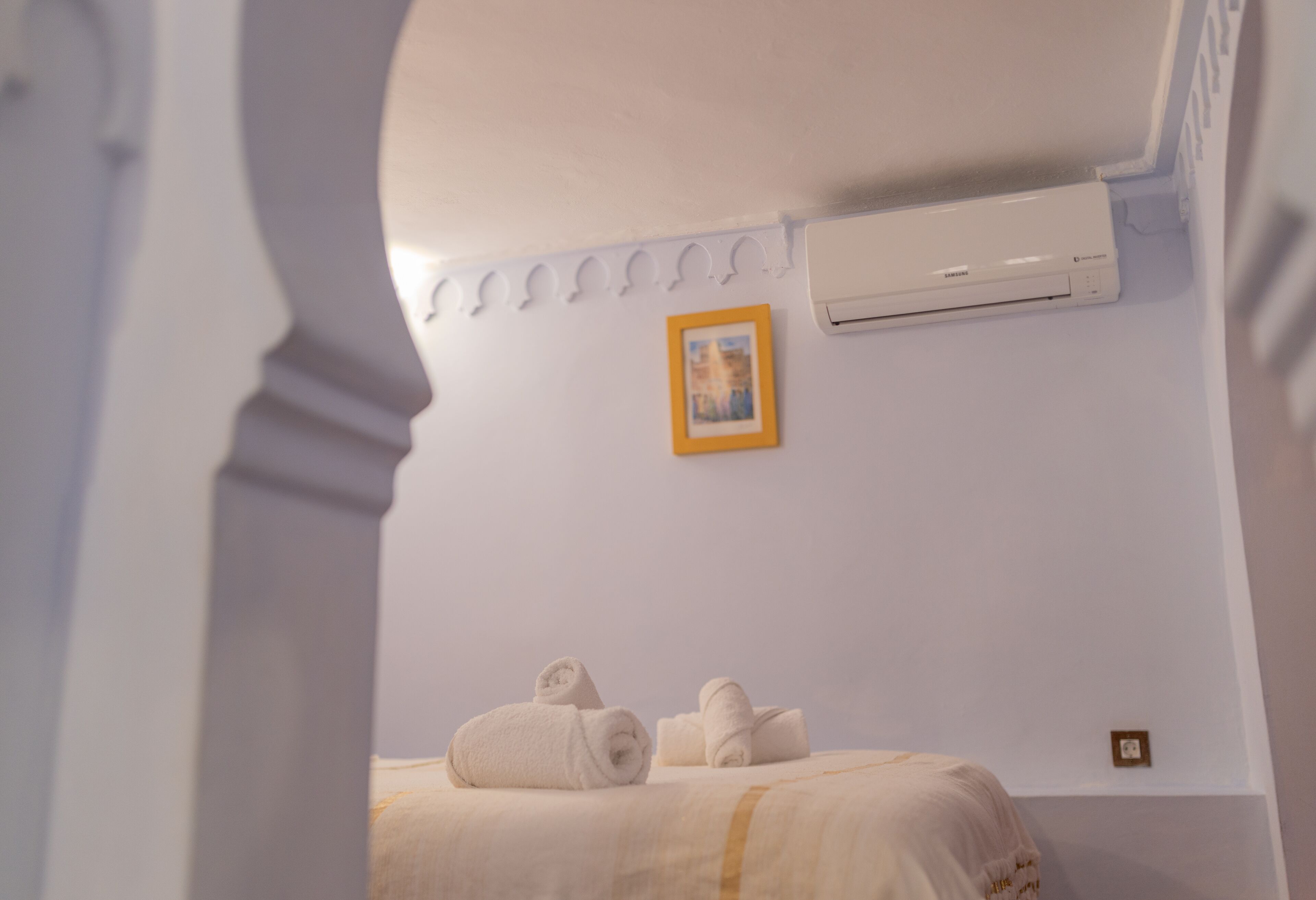 A hotel room with a bed, towels, an air conditioning unit, and a framed picture on the wall.
