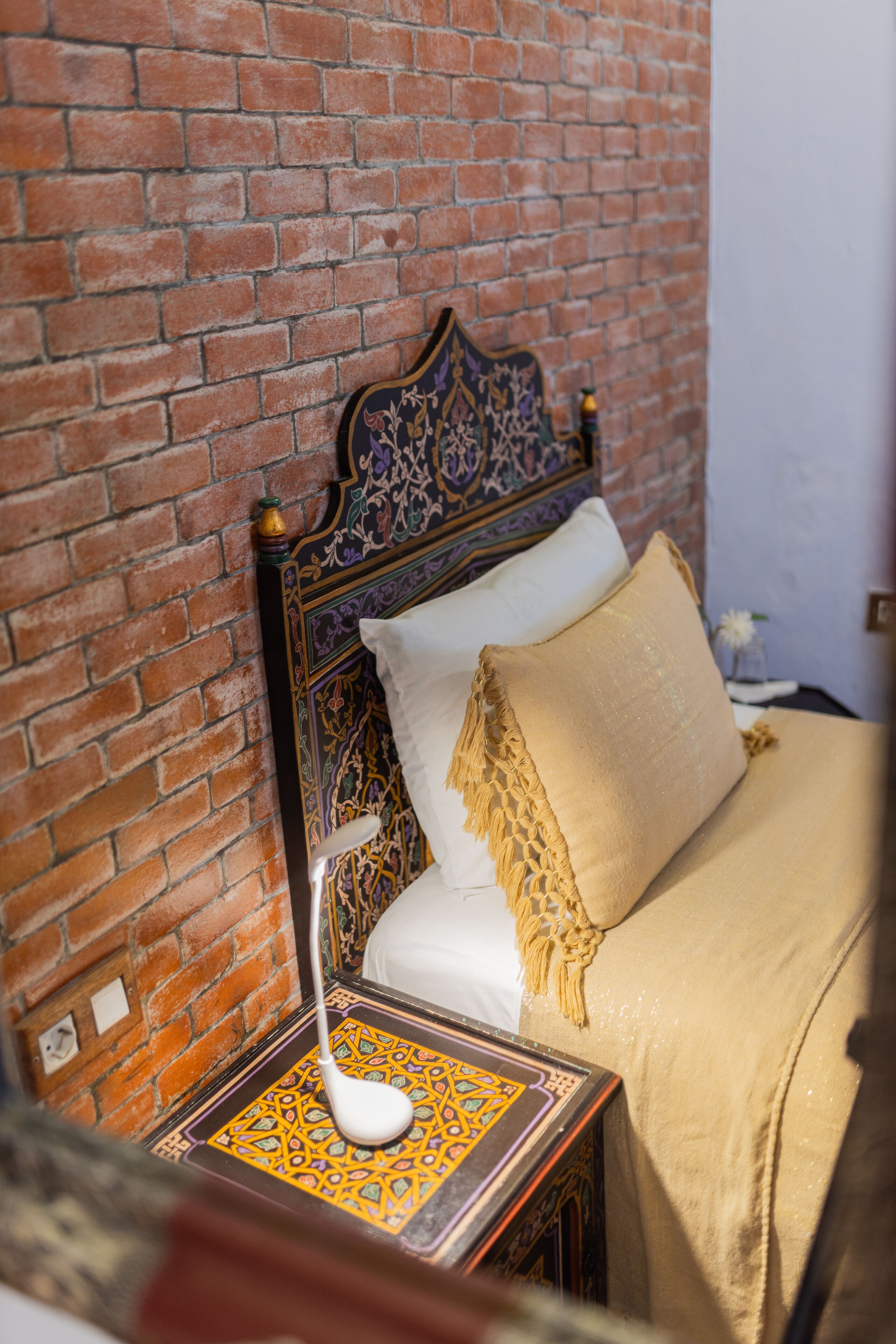 A bed with a patterned headboard, a bedside table with a lamp, and a brick wall.