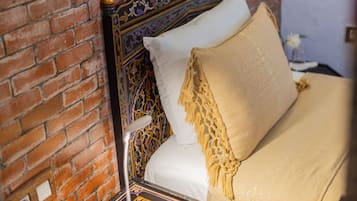 Una cama con cabecera estampada, una mesita de noche con lámpara y una pared de ladrillo.