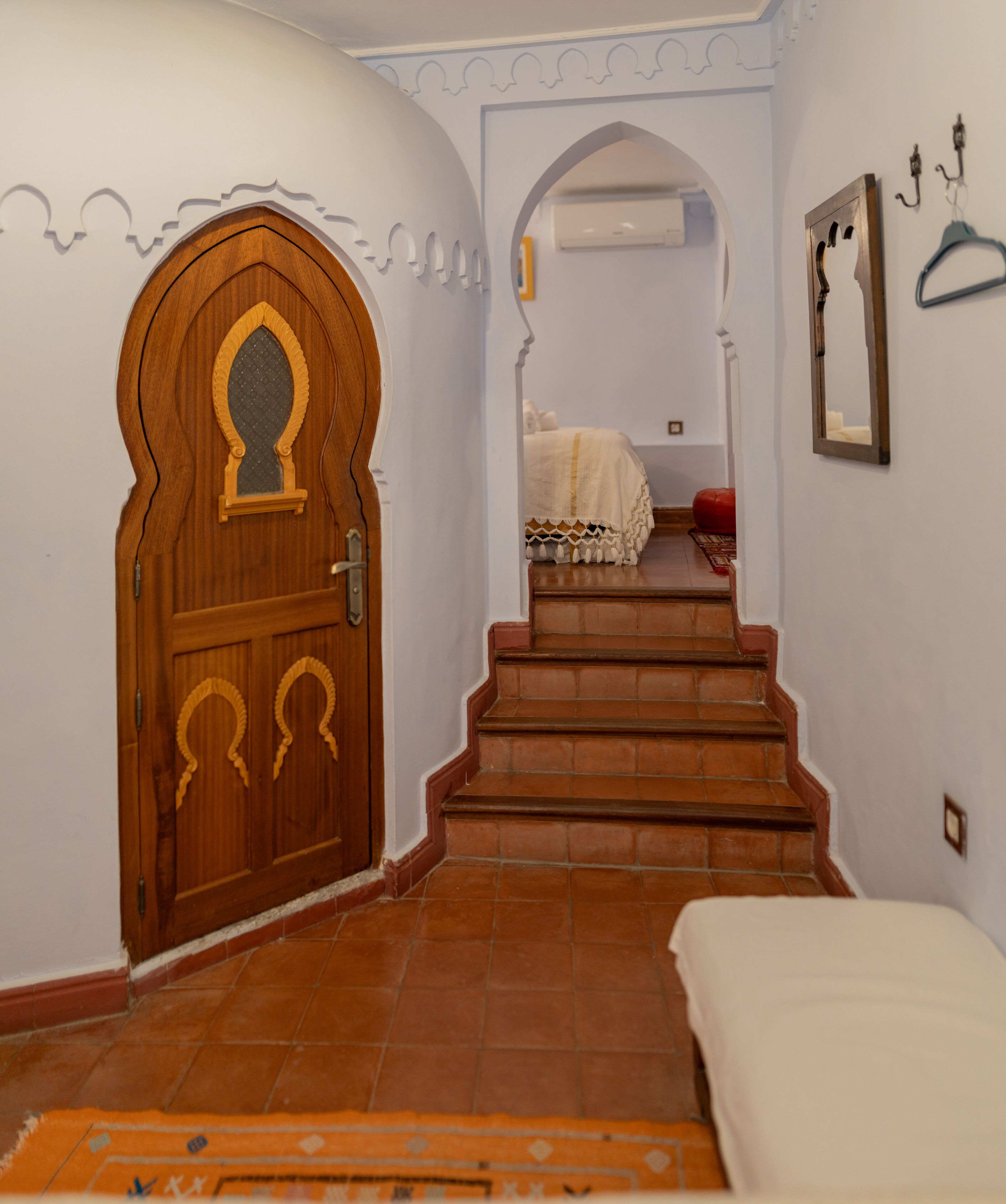 A hallway with a wooden door, a staircase, and a bed in the room.
