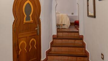 A hallway with a wooden door, a staircase, and a bed in the room.